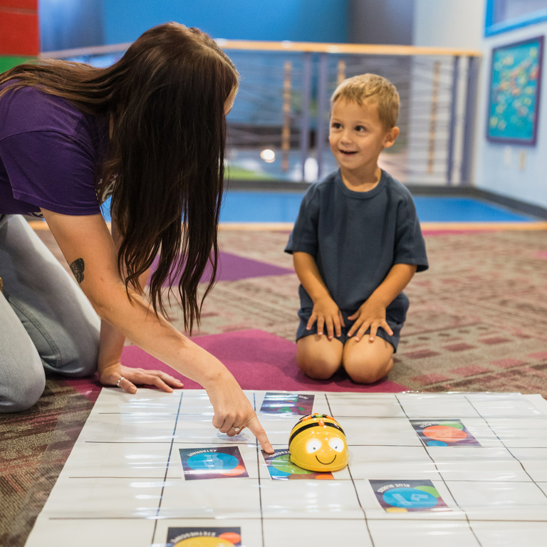 Museum employee engaging with student using Bee Bots